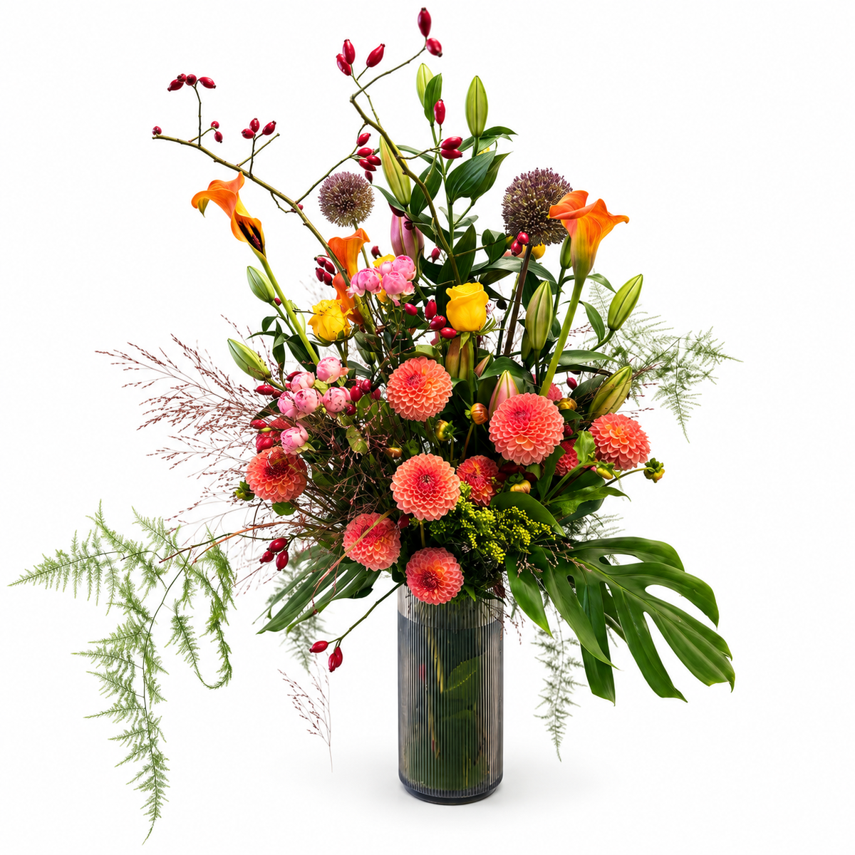 Hoge bloemencompositie in oranje, roze en geel met sierlijke takken en groen in een donkere geribbelde vaas.
