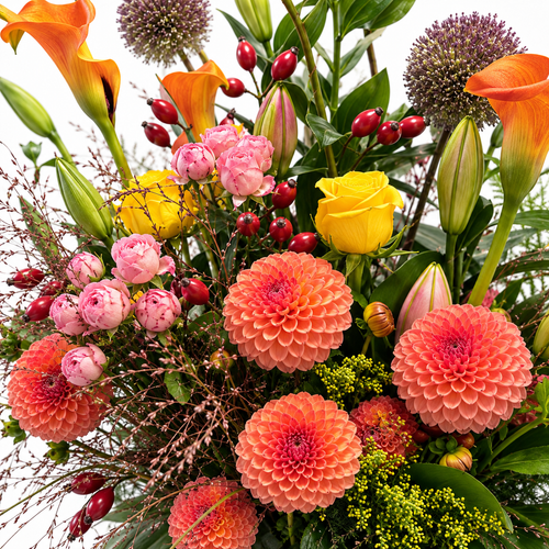 Detail van de oranje, roze en gele bloemen met rode bessen, fijne grassen en groen in bloemencompositie Ambra.